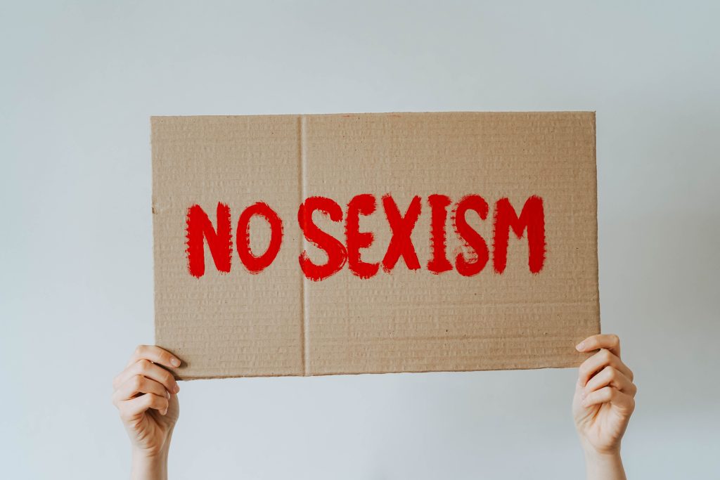 someone holding a cardboard sign with the words no sexism written in red